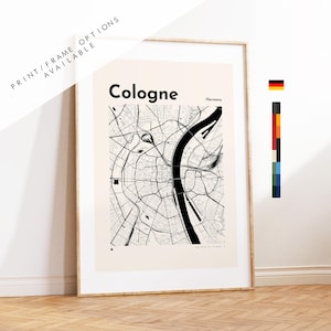 May include: A framed print featuring a black and white map of Cologne, Germany. The city name is displayed in bold black text. The print is in a light wood frame and is leaning against a white wall. The text 'Print/Frame Options Available' is visible.
