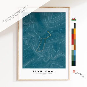 May include: A teal blue topographic map print of Llyn Idwal, a circular walk in Eryri, Wales. The print is framed in a light wood frame.