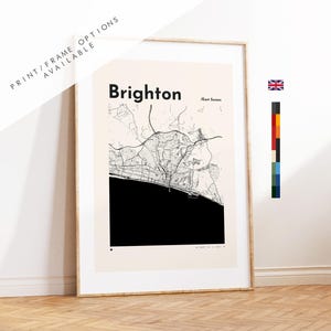 Op de afbeelding: Een ingelijste kunstdruk met een zwart-witte kaart van Brighton, East Sussex. De kaart toont gedetailleerde straatpatronen met een massief zwart vlak dat de zee voorstelt, geplaatst op een lichtcrèmekleurige achtergrond met de tekst Brighton.