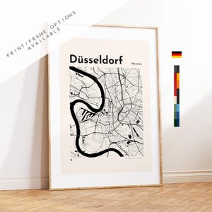 Peut inclure: Impression encadrée d'une carte en noir et blanc de Düsseldorf, Allemagne. Le nom de la ville est affiché en gras au-dessus de la carte. Le texte "PRINT/FRAME OPTIONS AVAILABLE" est en haut à gauche. L'impression est dans un cadre en bois clair.