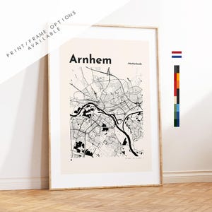 Op de afbeelding: Een ingelijste kaartafdruk van Arnhem, Nederland, in zwart en wit. De kaart toont de indeling van de stad, inclusief wegen en waterwegen. De tekst "Arnhem" staat bovenaan, met "Print/Frame Options Available" linksboven.