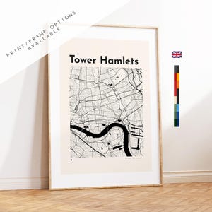 May include: A framed wall art print featuring a black and white map of Tower Hamlets, London. The map displays a detailed street grid and a prominent river section on a cream-colored background. The text "Tower Hamlets" is printed in black at the top.