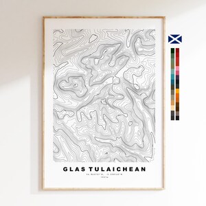 May include: A framed topographic map print of Glas Tulaichean featuring black contour lines on a white background. The text reads GLAS TULAICHEAN, 56.865757°N, -3.558143°W, and 1051m. A small Scottish flag and a vertical colour palette are on the right.