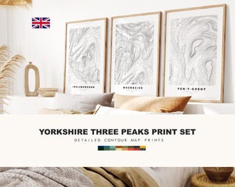 May include: A set of three framed wall art prints featuring detailed black and white contour maps of Ingleborough, Whernside, and Pen-y-ghent. Each print displays topographic lines and the mountain name at the bottom, presented in light wood frames.