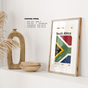 May include: A framed print of the South African flag with a white background and the text "South Africa" in black. The flag is red, yellow, green, and blue. The print is in a wooden frame.