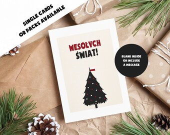 Può includere: Un biglietto di Natale con un design di albero di Natale nero e rosso e il testo polacco "Wesołych Świąt!" in rosso e nero. Il biglietto è su uno sfondo beige con una busta marrone, aghi di pino e regali confezionati.