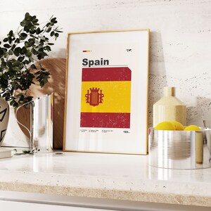 K&ouml;nnte beinhalten: Ein gerahmter Druck mit wei&szlig;em Hintergrund und dem Wort "Spanien" in schwarzem Text. Der Druck zeigt eine rot-gelbe Flagge mit einem Wappen in der Mitte. Die Flagge hat einen abgenutzten, Vintage-Look.