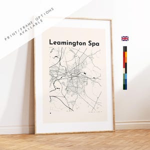 May include: A framed wall art print featuring a black line map of Leamington Spa on a light beige background. The text Leamington Spa is printed in black at the top. A small Union Jack flag and a vertical colour palette bar are visible on the right.