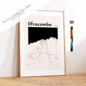 May include: A framed wall art print featuring a map of Ilfracombe, Devon. The design displays the town name in bold black text above a black silhouette of the coastline and a detailed network of thin black road lines on a light cream background.