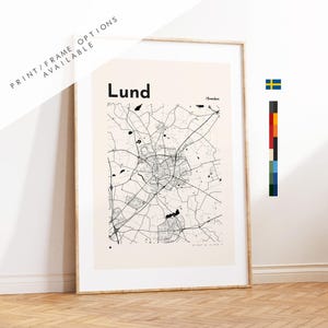 May include: A framed wall art print featuring a black and white map of Lund, Sweden. The map displays intricate street networks on a light beige background. The text "Lund" and "Sweden" are printed at the top. A small Swedish flag icon is visible.