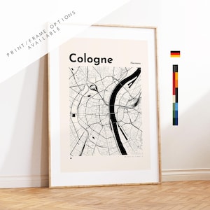 May include: A framed wall art print featuring a black and white map of Cologne, Germany, with the text Cologne and /Germany printed at the top. The map displays a detailed street grid and the Rhine River in black lines against a cream background.