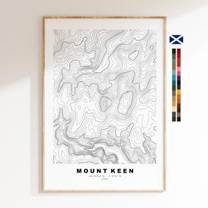 May include: A framed topographic map print of Mount Keen featuring black contour lines on a white background. The text reads MOUNT KEEN, 56.96952°N, -3.0737°W, 939m. A vertical color palette strip is positioned to the right of the main print.