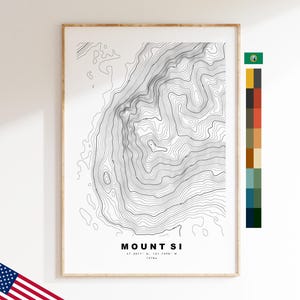 Op de afbeelding: Een ingelijste topografische kaartafdruk van Mount Si met zwarte hoogtelijnen op een witte achtergrond. De tekst luidt MOUNT SI, 47.5077 N, 121.7399 W, 1276m. Rechts staat een verticale kleurpaletstrook en bovenaan een klein vlagpictogram.