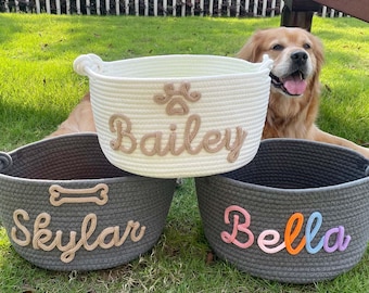 May include: Three woven rope pet baskets in white and gray. The white basket has the name "Bailey" embroidered in beige, with a paw print design. The gray baskets are labeled "Skylar" and "Bella" in beige and colorful letters.