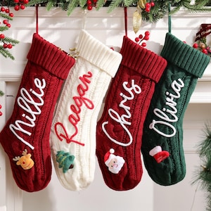May include: Four personalized Christmas stockings hang from a white mantel. The stockings are red, white, and green, with names embroidered in white. Each stocking has a festive applique, including a reindeer, Christmas tree, Santa, and a stocking.