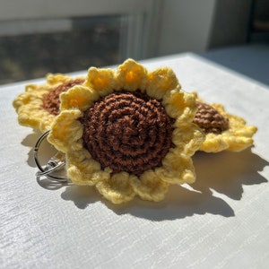 May include: Two crocheted sunflower keychains with brown centers and yellow petals. The keychains are attached to a silver key ring.