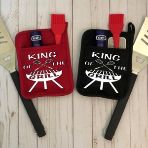 May include: Two red and black oven mitts with the text "King of the Grill" and a grill graphic. Each mitt has a pocket for grilling tools, and a spatula and brush are included.