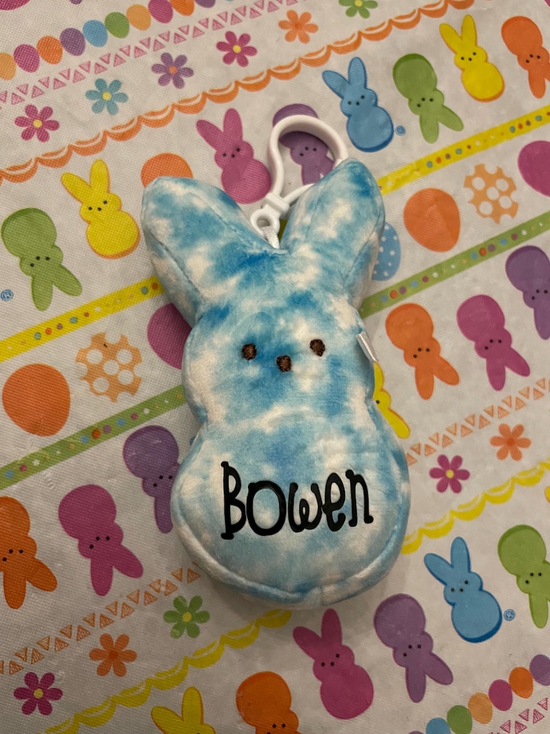 May include: A blue and white tie-dye plush bunny with a black embroidered name "Bowen" on the front. The bunny is attached to a white plastic key chain.