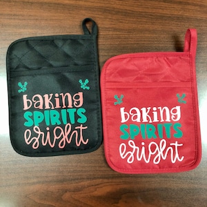 May include: Two quilted oven mitts with a Christmas theme. One is black with pink and green text that says "baking spirits bright". The other is red with white text that says "baking spirits bright".