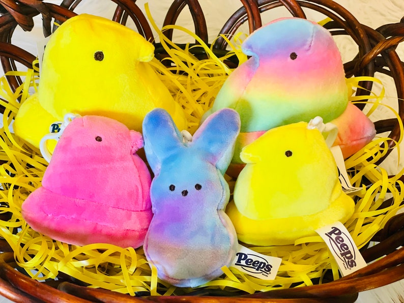 May include: Five colorful plush Peep chicks in a wicker basket filled with yellow shredded paper. The chicks are yellow, pink, blue, and rainbow. The chicks have the word "Peeps" on their tags.