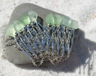 May include: A silver hair comb with a chain and five sea glass pieces attached. The sea glass is light green and translucent.