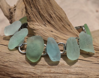 May include: A bracelet made with sea glass and silver chain links. The sea glass is a light green color.