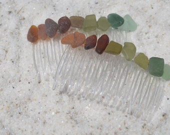 May include: A clear plastic comb with a row of sea glass pieces in shades of brown, green, and blue. The sea glass is arranged in a rainbow pattern.