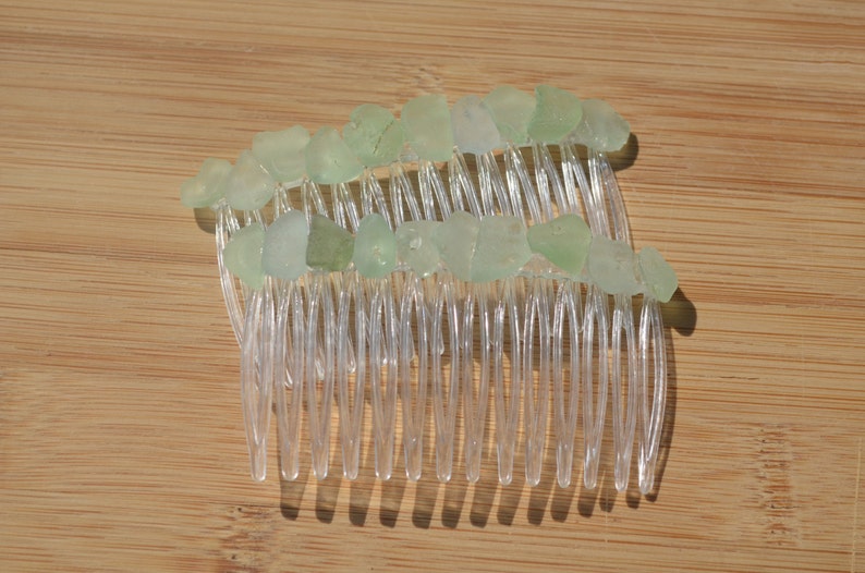 May include: A clear plastic hair comb with light green sea glass pieces attached to the teeth.