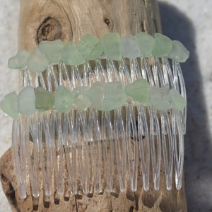 May include: A clear plastic hair comb with two rows of light green sea glass pieces attached to the top.