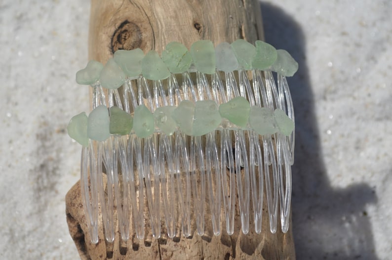 May include: A clear plastic hair comb with two rows of light green sea glass pieces attached to the top.