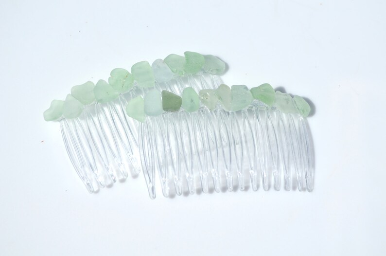 May include: Two clear plastic hair combs with light green sea glass pieces attached to the top of each comb.