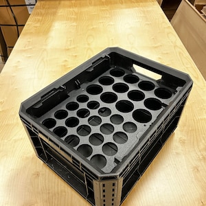 May include: Black plastic crate with circular cutouts for holding items. The crate has a textured surface and is designed for stacking.