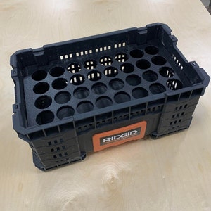 K&ouml;nnte beinhalten: Schwarze Plastik-Aufbewahrungsbox mit einem roten und schwarzen RIDGID-Etikett. Die Box hat ein Gittermuster und einen herausnehmbaren Einsatz mit 24 runden L&ouml;chern.