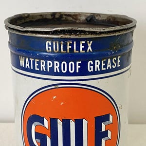 May include: A vintage Gulflex Waterproof Grease tin. The tin is white with a blue band at the top and an orange circle with the Gulf logo. The text "GULFFLEX WATERPROOF GREASE" is printed on the tin.