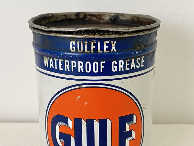 May include: A vintage Gulflex Waterproof Grease tin. The tin is white with a blue band at the top and an orange circle with the Gulf logo. The text "GULFFLEX WATERPROOF GREASE" is printed on the tin.