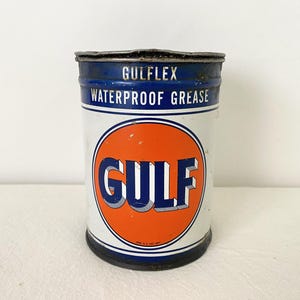 May include: A vintage Gulflex waterproof grease tin. The cylindrical tin has a white body with blue bands at the top and bottom. The Gulf logo is in an orange circle. The text "WATERPROOF GREASE" is printed on the tin.