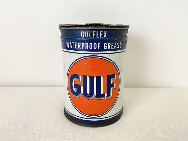 May include: A vintage Gulflex waterproof grease tin. The cylindrical tin has a white body with blue bands at the top and bottom. The Gulf logo is in an orange circle. The text "WATERPROOF GREASE" is printed on the tin.