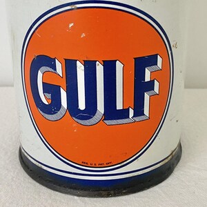May include: A vintage metal can featuring the "GULF" logo in blue and white on an orange circle. The can has a white background with a blue and white border. The base of the can is black.