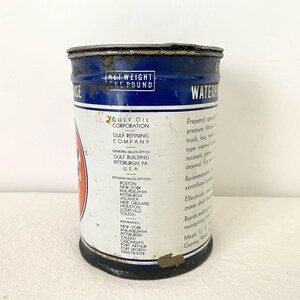 May include: A vintage Gulf Oil Corporation grease tin. The cylindrical metal container has a blue top and base with white and red details. Text includes "Net Weight One Pound" and "Waterproof Grease".