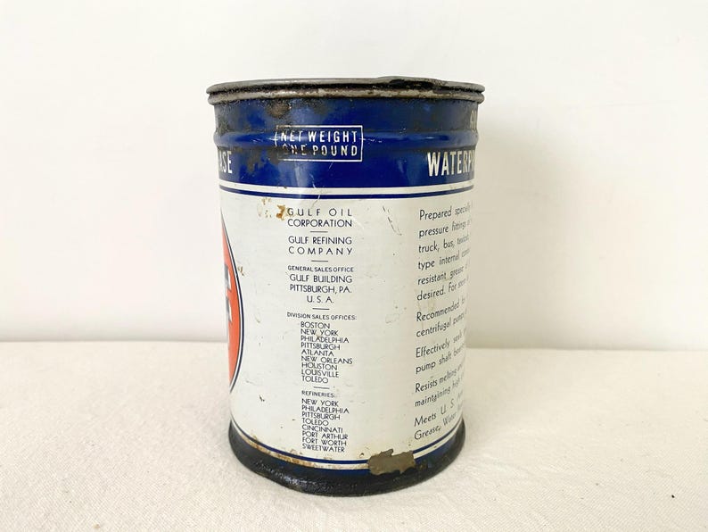 May include: A vintage Gulf Oil Corporation grease tin. The cylindrical metal container has a blue top and base with white and red details. Text includes "Net Weight One Pound" and "Waterproof Grease".