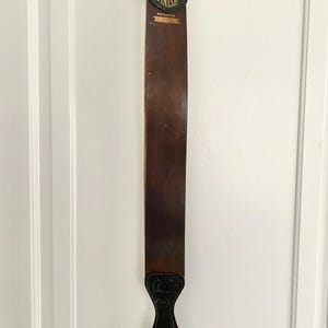 May include: A vintage leather strop for sharpening straight razors. The strop is brown with a black handle and a metal ring for hanging. The text "FINISH" and "GENUINE SHELL" are printed in gold lettering on the leather.