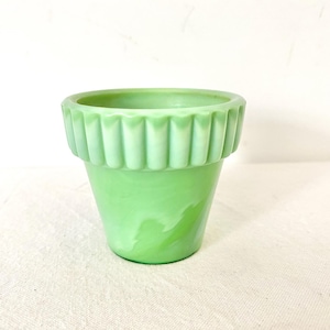 May include: A light green marbled glass planter with a smooth, tapered body and a wide, fluted rim. The glass features a swirling pattern of lighter and darker green tones throughout the surface, creating a distinct, semi-translucent appearance.