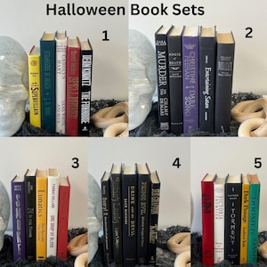 May include: Five sets of Halloween themed books stacked on top of each other. Each set is arranged on a white skull with a black background. The books are all different colors and have titles like "Murder on the Champ de Mars", "The Funhouse", "One Drop of Blood", "Drink with the Devil", and "Doomed Oasis".
