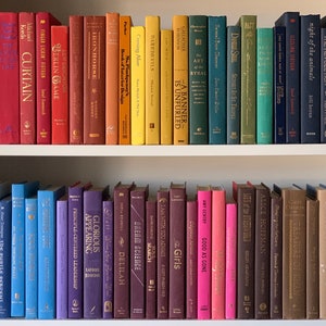 May include: A bookshelf filled with colorful hardcover books. The books are arranged in rows, with the spines facing out. The books are all different sizes and shapes, and they have a variety of titles and authors. The bookshelf is made of wood and has a white finish.