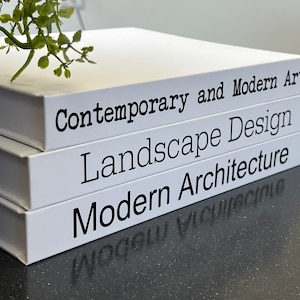 May include: Three white books stacked on top of each other. The titles of the books are "Contemporary and Modern Art", "Landscape Design", and "Modern Architecture".