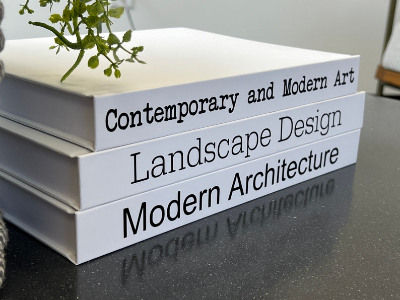 May include: Three white books stacked on top of each other. The titles of the books are "Contemporary and Modern Art", "Landscape Design", and "Modern Architecture".