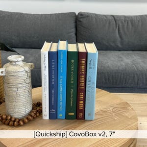 May include: A collection of six hardcover books with various colored spines, including blue, green, and burgundy. The titles and authors are visible, with text such as "House of Gold" and "Special Characters". The books are arranged on a wooden table.