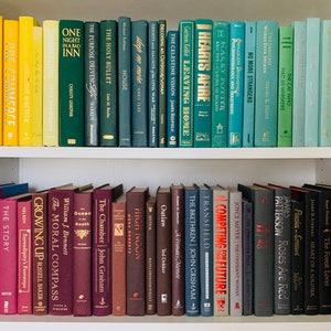 May include: A bookshelf with two rows of books. The top row has books with green, blue, and yellow spines. The bottom row has books with red, brown, and black spines. The titles of some of the books are visible, including "The Moral Compass", "The Chamber", "Competing for the Future", and "Roses Are Red".
