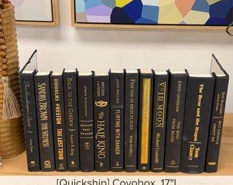 May include: A collection of twelve black books with gold lettering on the spines, arranged upright in a row. The titles include The Housekeeper's Secret, The Witness, The Lost Tomb, Back to the Garden, Knowing What We Know, The Half King, and others.