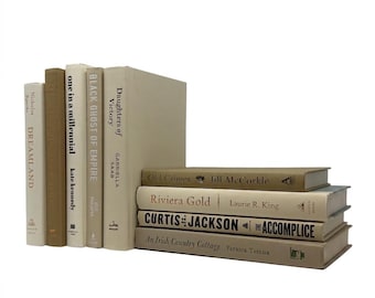 May include: A collection of nine hardcover books arranged in a stack and a row. Five books stand vertically in neutral beige and tan tones, while four books are stacked horizontally, featuring titles like Dreamland, Riviera Gold, and Curtis & Jackson.